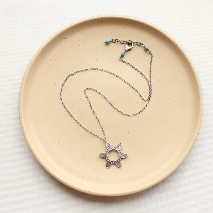 The feathered sun necklace styled on a tan plate to show the adjustable lobster clasp closure