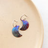 The fire painted copper moon earrings styled on a tan plate