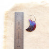A fire painted copper moon earring next to a ruler for size reference