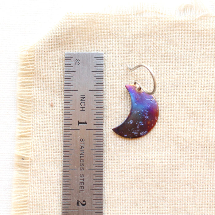 A fire painted copper moon earring next to a ruler for size reference