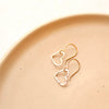 The gold floating heart earrings styled on tan linen
