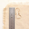 A gold floating heart earring next to a ruler for size reference