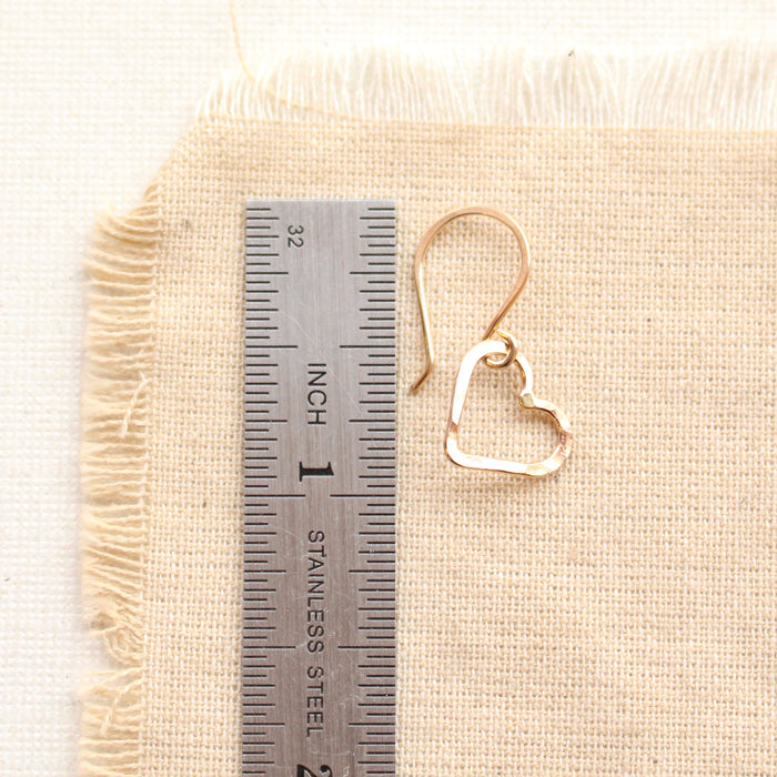 A gold floating heart earring next to a ruler for size reference