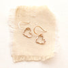 The gold floating heart earrings styled on tan linen