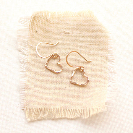 The gold floating heart earrings styled on tan linen