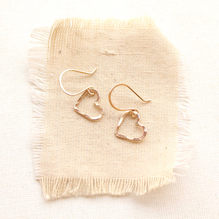 The gold floating heart earrings styled on tan linen