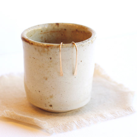 The gold hook earrings styled on a ceramic cup 