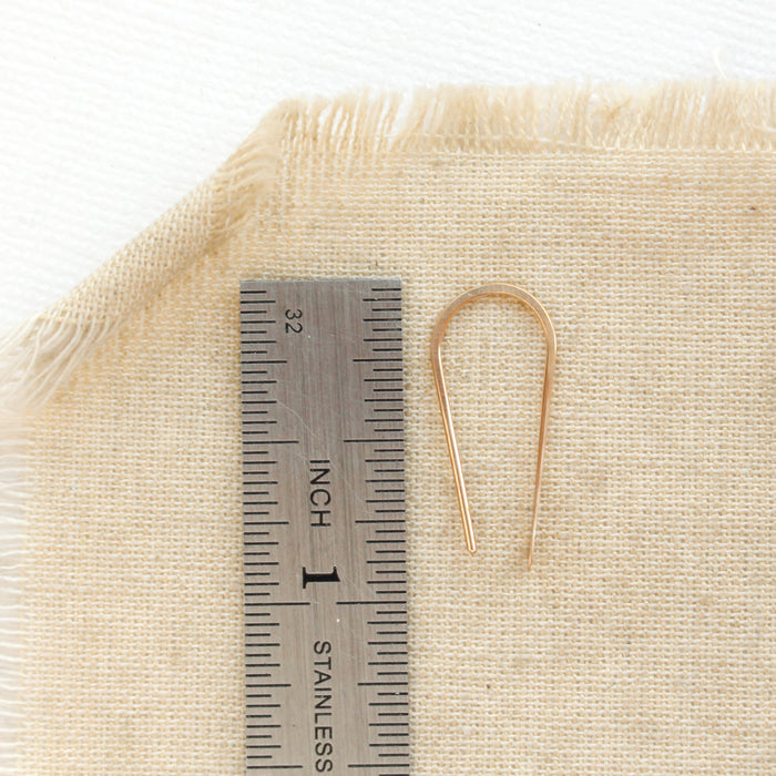 A gold hook earring next to a ruler for size reference