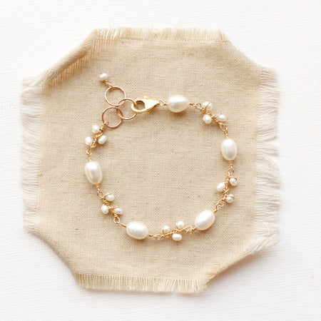 The gold pearl bud vine bracelet styled on tan linen
