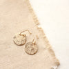 The gold raw silk disc earrings styled on tan linen