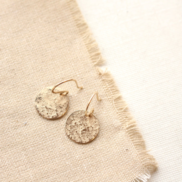 The gold raw silk disc earrings styled on tan linen