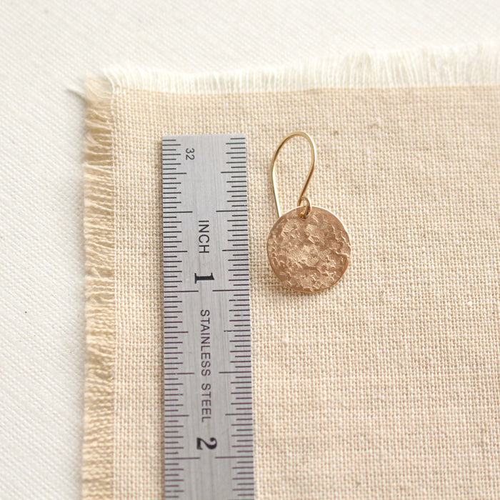 A raw silk disc earring next to a ruler for size reference