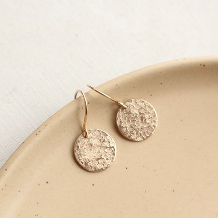 The gold raw silk disc earrings styled on a tan plate
