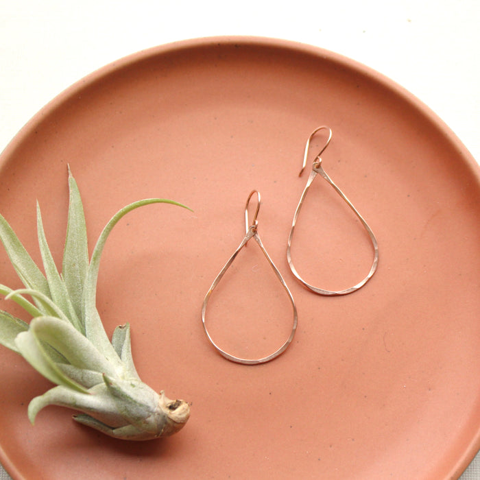 The rose gold fill forged teardrop hoop earrings styled on an orange plate with an air plant