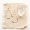 The yellow gold fill forged teardrop hoop earrings styled on tan linen with a crystal
