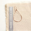A rose gold fill forged teardrop hoop earring next to a ruler for size reference