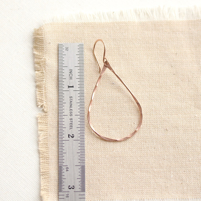 A rose gold fill forged teardrop hoop earring next to a ruler for size reference