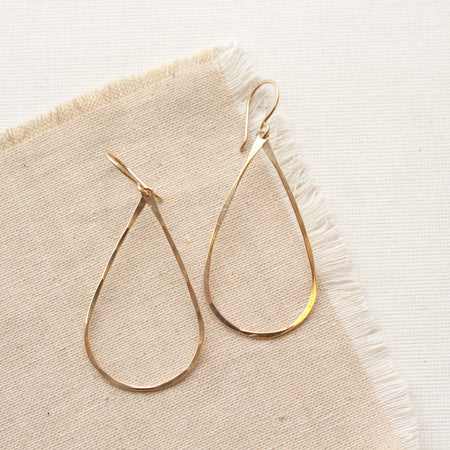 The yellow gold fill forged teardrop hoop earrings styled on tan linen