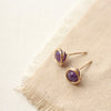 The gold wrapped amethyst post earrings styled on tan linen