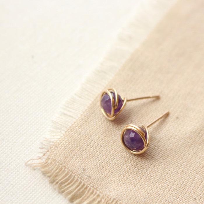 The gold wrapped amethyst post earrings styled on tan linen