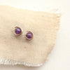 The gold wrapped amethyst post earrings styled on tan linen