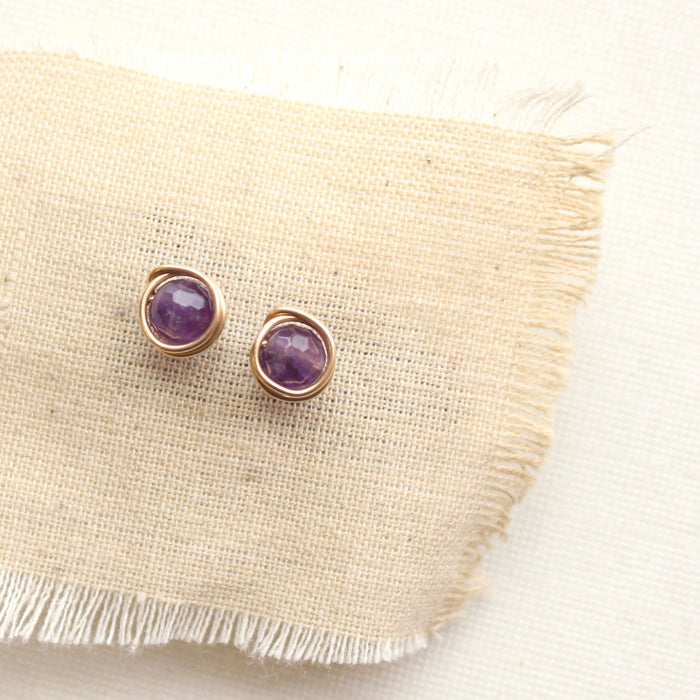 The gold wrapped amethyst post earrings styled on tan linen