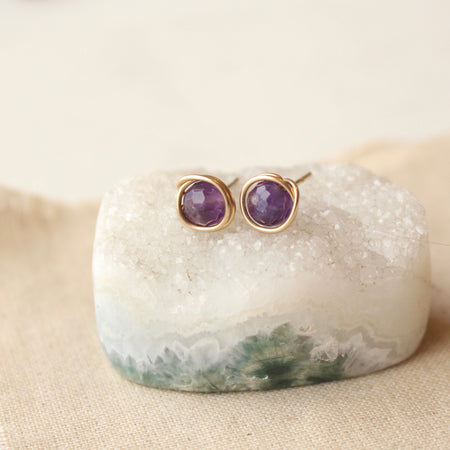 The gold wrapped amethyst post earrings styled on a crystal with linen