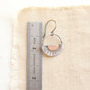 A happy half sun earring next to a ruler for size reference