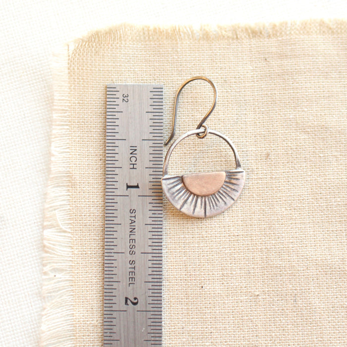 A happy half sun earring next to a ruler for size reference