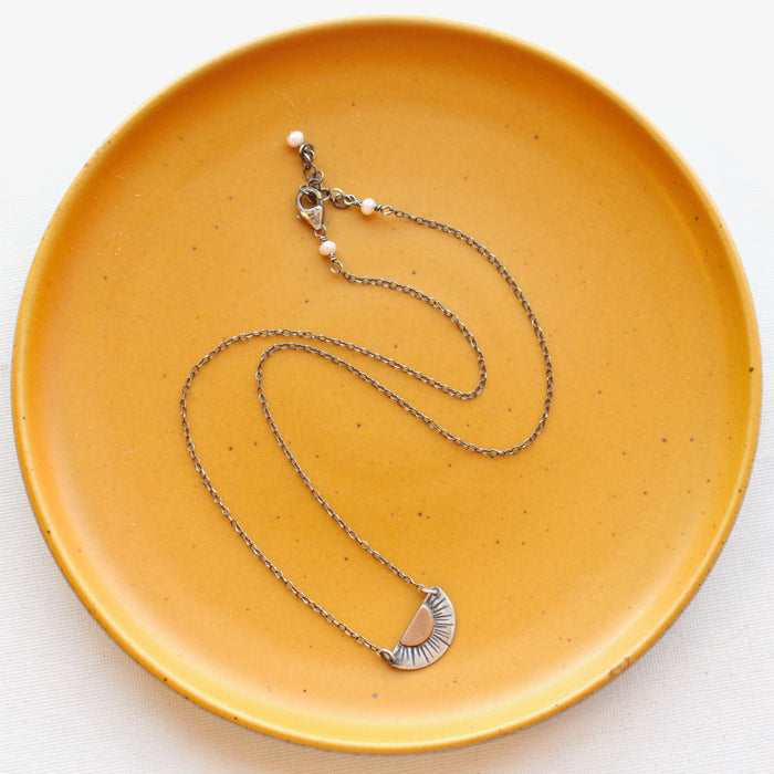 The happy half sun necklace styled on a yellow plate to show the adjustable lobster clasp closure