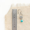 A turquoise jolie earring next to a ruler for size reference