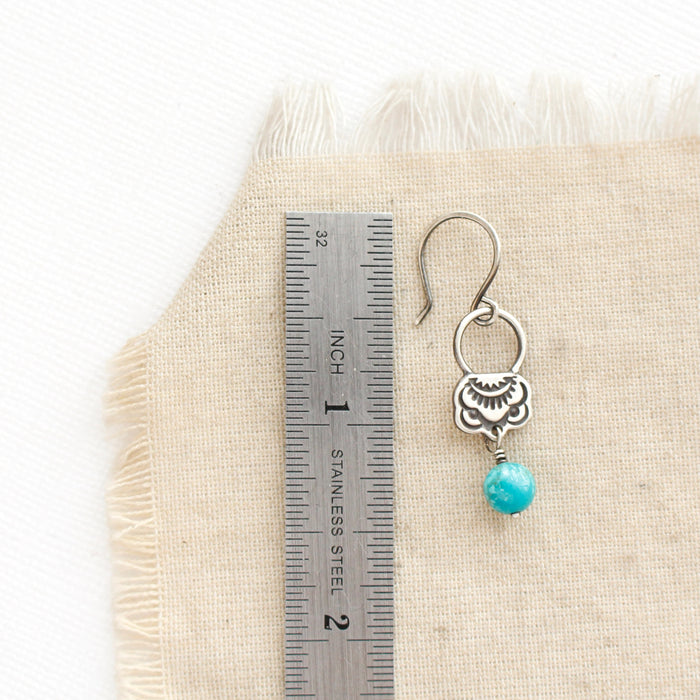 A turquoise jolie earring next to a ruler for size reference