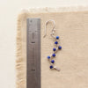 A lapis wrapped silver vine earring next to a ruler for size reference