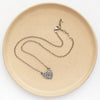 The layers of love heart necklace styled on a tan plate to show the adjustable lobster clasp closure