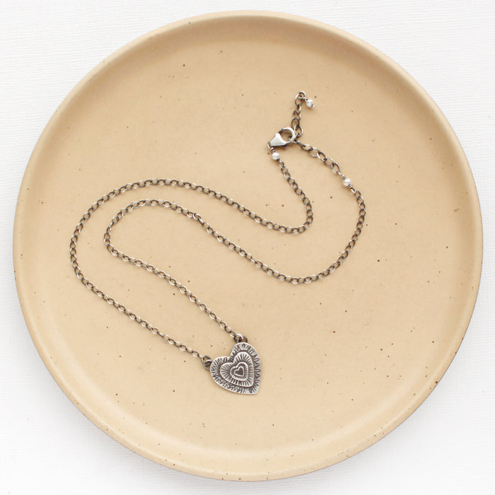 The layers of love heart necklace styled on a tan plate to show the adjustable lobster clasp closure