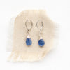 The kyanite drop earrings styled on tan linen