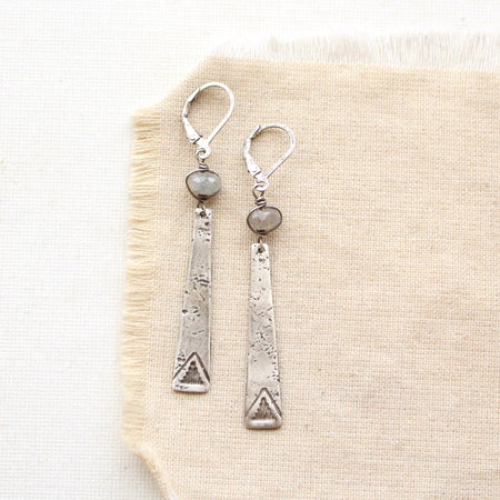 Long stamped silver triangles with labradorite stones earrings styled on tan linen.