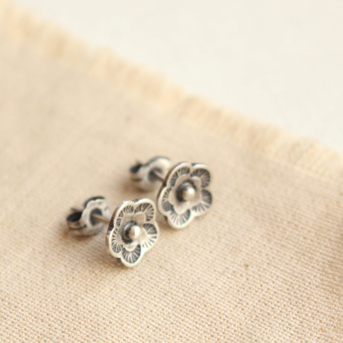 The mini cactus flower post earrings styled on tan linen