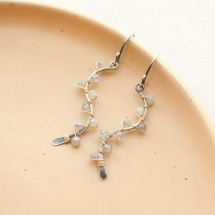 The labradorite wrapped mixed metal vine earrings styled on a tan plate