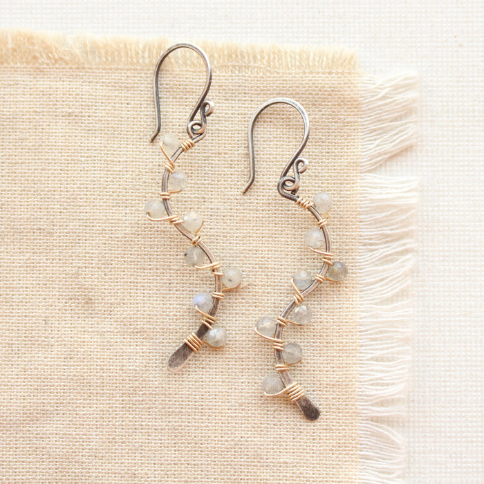 labradorite wrapped with gold around delicate silver vines styled on tan linen