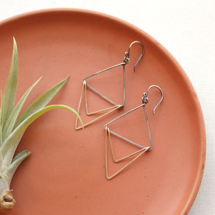The mixed metal triple triangle hoop earrings styled on an orange plate with an airplant