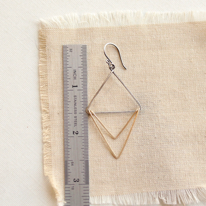 A mixed metal triple triangle hoop earring next to a ruler for size reference