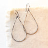 The oxidized silver forged teardrop hoop earrings styled on tan linen