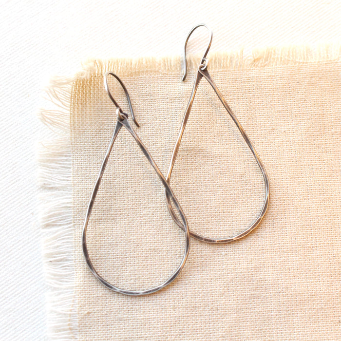 The oxidized silver forged teardrop hoop earrings styled on tan linen