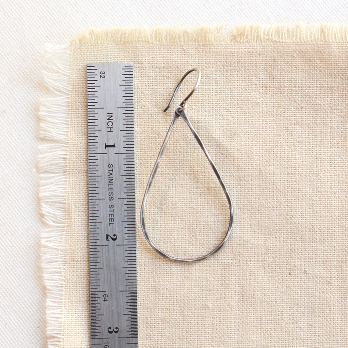 An oxidized silver forged teardrop hoop earring next to a ruler for size reference