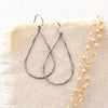 The oxidized silver forged teardrop hoop earrings styled on tan linen with dried grass