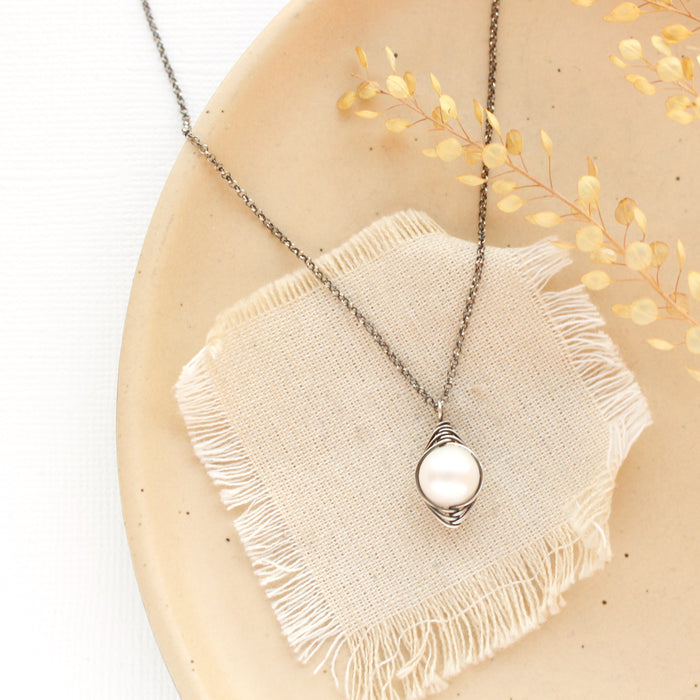 The oxidized silver perfect pearl necklace styled on a tan plate with linen and dried grass
