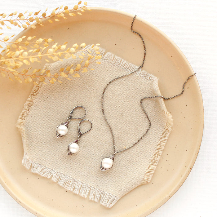 The oxidized silver perfect pearl necklace styled on a tan plate with the matching earrings