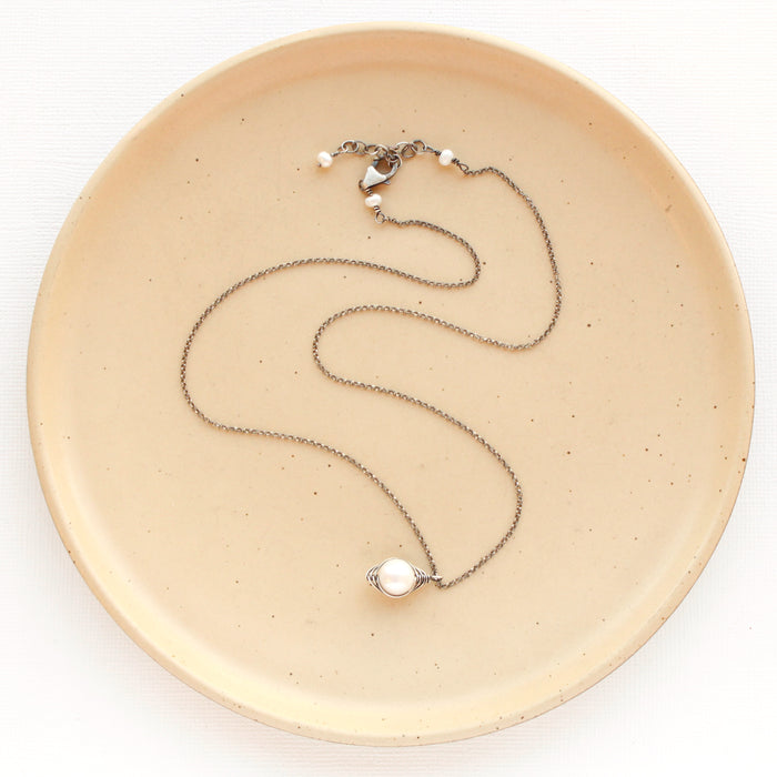 The oxidized silver perfect pearl necklace styled on a tan plate to show the adjustable lobster clasp closure