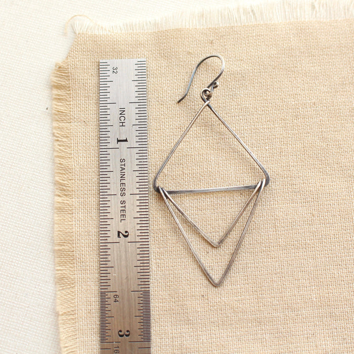 An oxidized silver triple triangle hoop earring next to a ruler for size reference